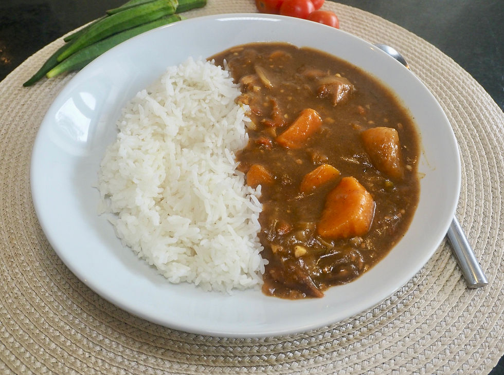 Plate of white rice with Chicken and Butternut curry and carrots on a placemat, with okra and tomatoes in the background.