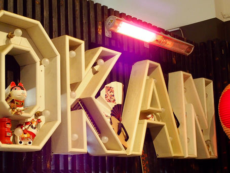 Decorative letters "OKAN" with figurines and lights against a dark wall, a red lantern and heater in the background, creating a cozy ambiance.