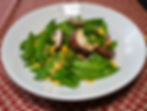 Stir fried sugar snap peas, mushrooms, and corn on a white plate, garnished with parsley. Set on a red and white patterned tablecloth.