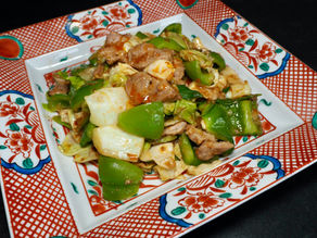 Stir-fried pork with cabbage and green bell peppers on a decorative red and white plate with floral patterns. Rich and appetizing.