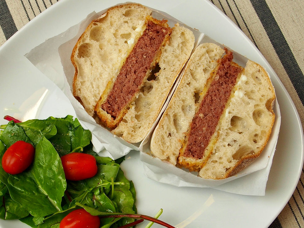 Halved sandwich with thick meat filling on a white plate beside spinach and cherry tomatoes on a striped cloth. Katsu sando.