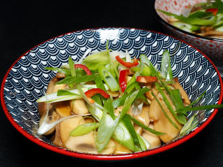 A bowl of stir-fried mushrooms with green onions and red peppers, in a patterned blue bowl with a red rim, on a dark background. donburi.