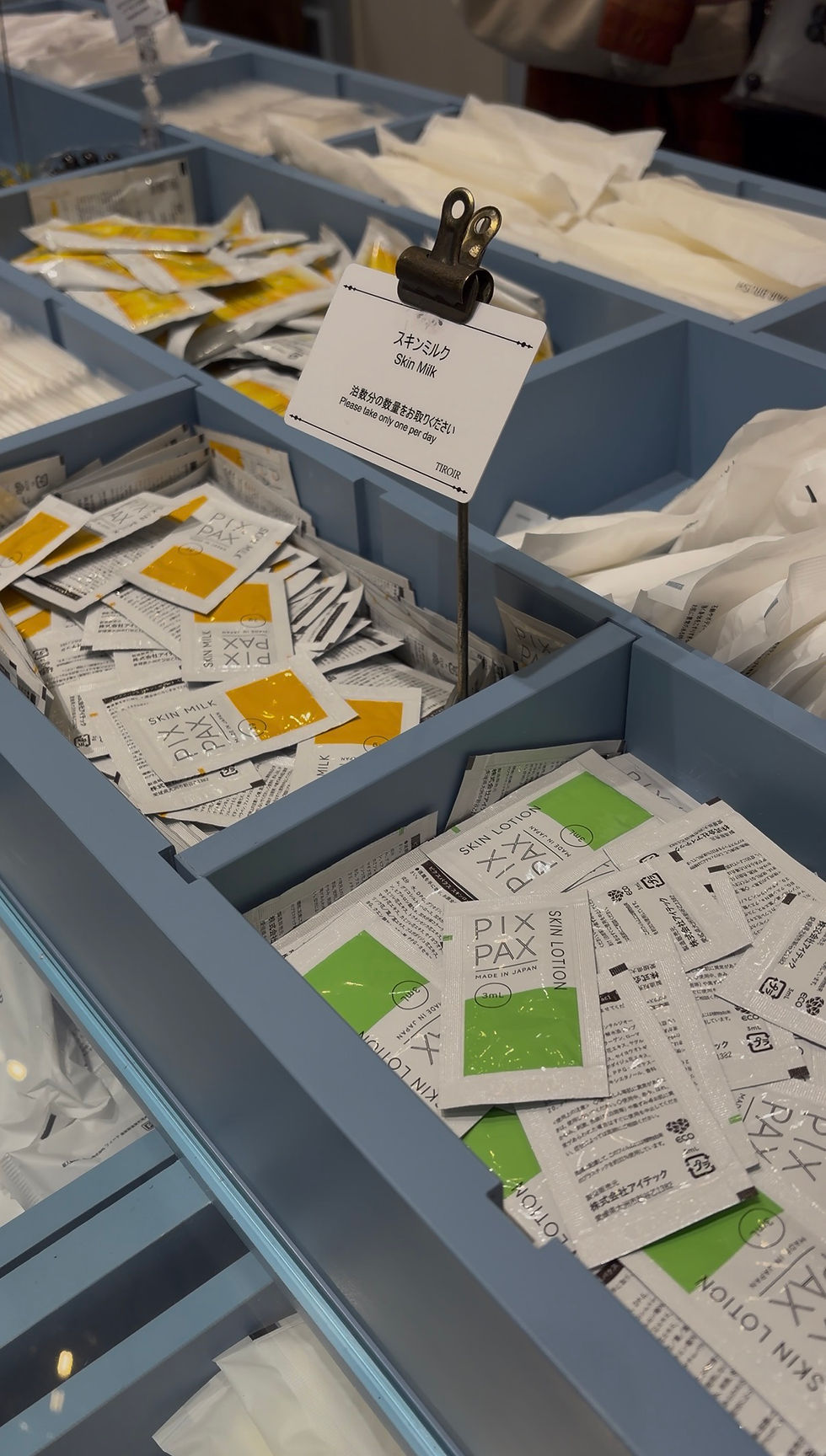 Packets of "Skin Milk" and "Skin Lotion" in blue trays. Labels read "Please take only one per day." Colors: yellow and green accents.