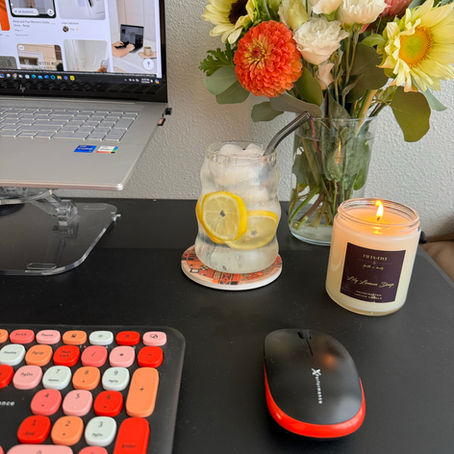 Colorful keyboard, mouse, and iced lemon drink on a desk with flowers, candle, and laptop displaying Pinterest. Cozy work setup.