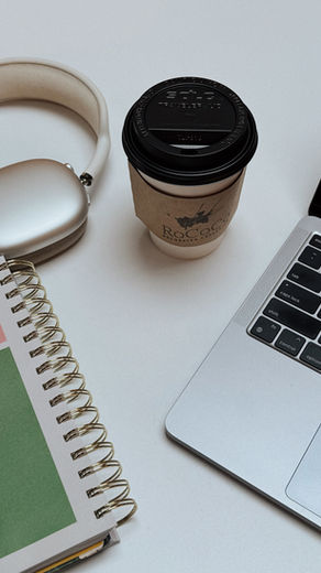 Laptop, headphones, colorful notebook, and coffee cup on a white desk. The cup reads "Rococo" and the mood is calm and focused.