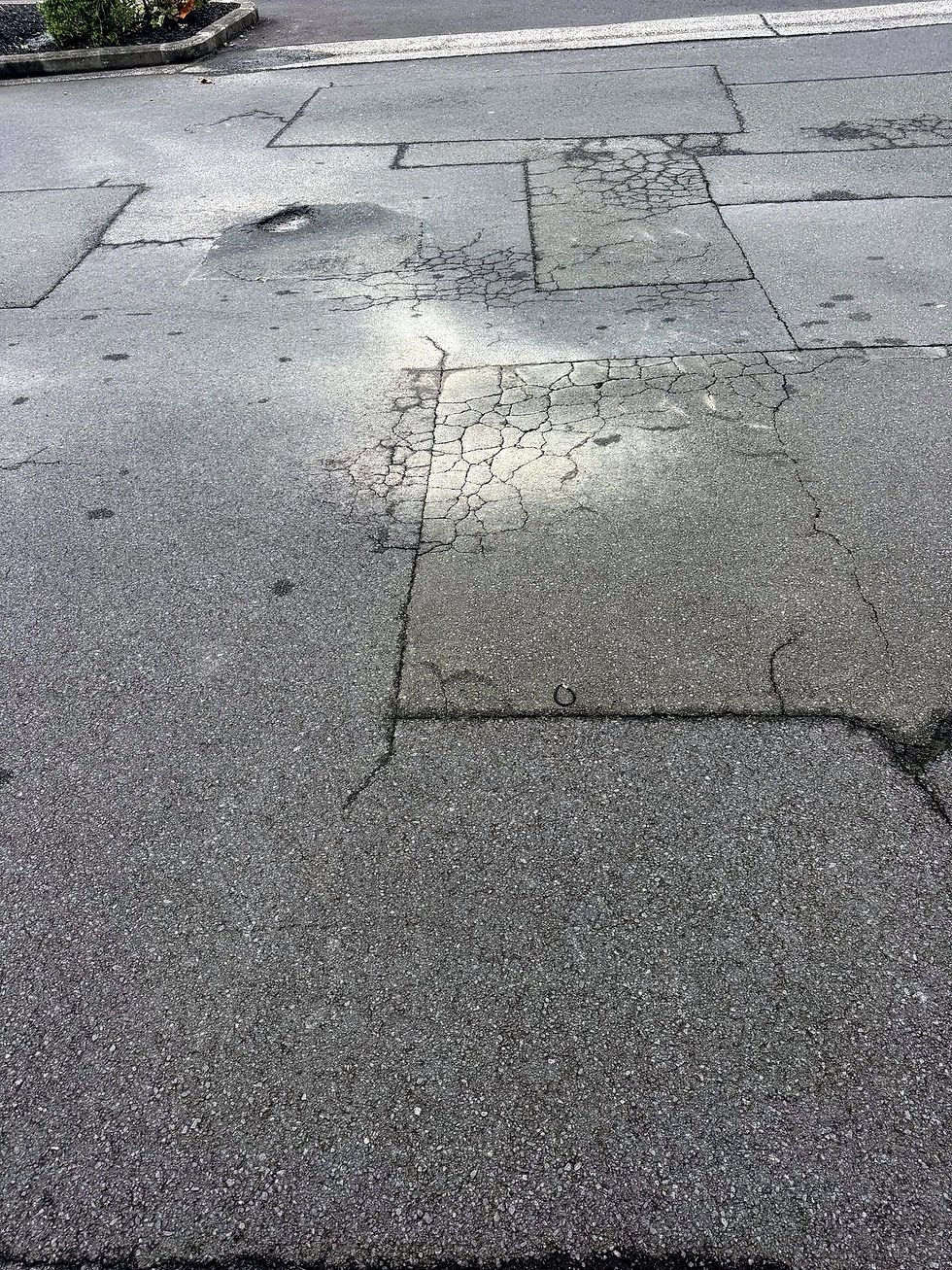 The crumbling edge of a forming pothole in Auckland asphalt.