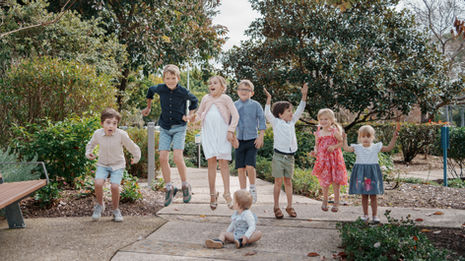 Large extended family group portrait at Gold Coast Regional Botanic Gardens featuring coordinated colorful outfits and a lush green backdrop.