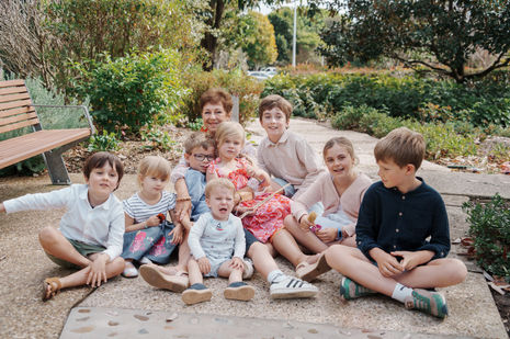 Large extended family group portrait at Gold Coast Regional Botanic Gardens featuring coordinated colorful outfits and a lush green backdrop.