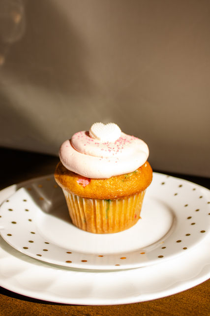 Funfetti cupcake with vanilla pink buttercream frosting and heart topping on a plate.