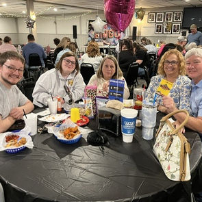 Five people are seated around a round table and a few of them are eating as the others are talking. They appear to be having a great time visiting with each other during a break in the bingo.