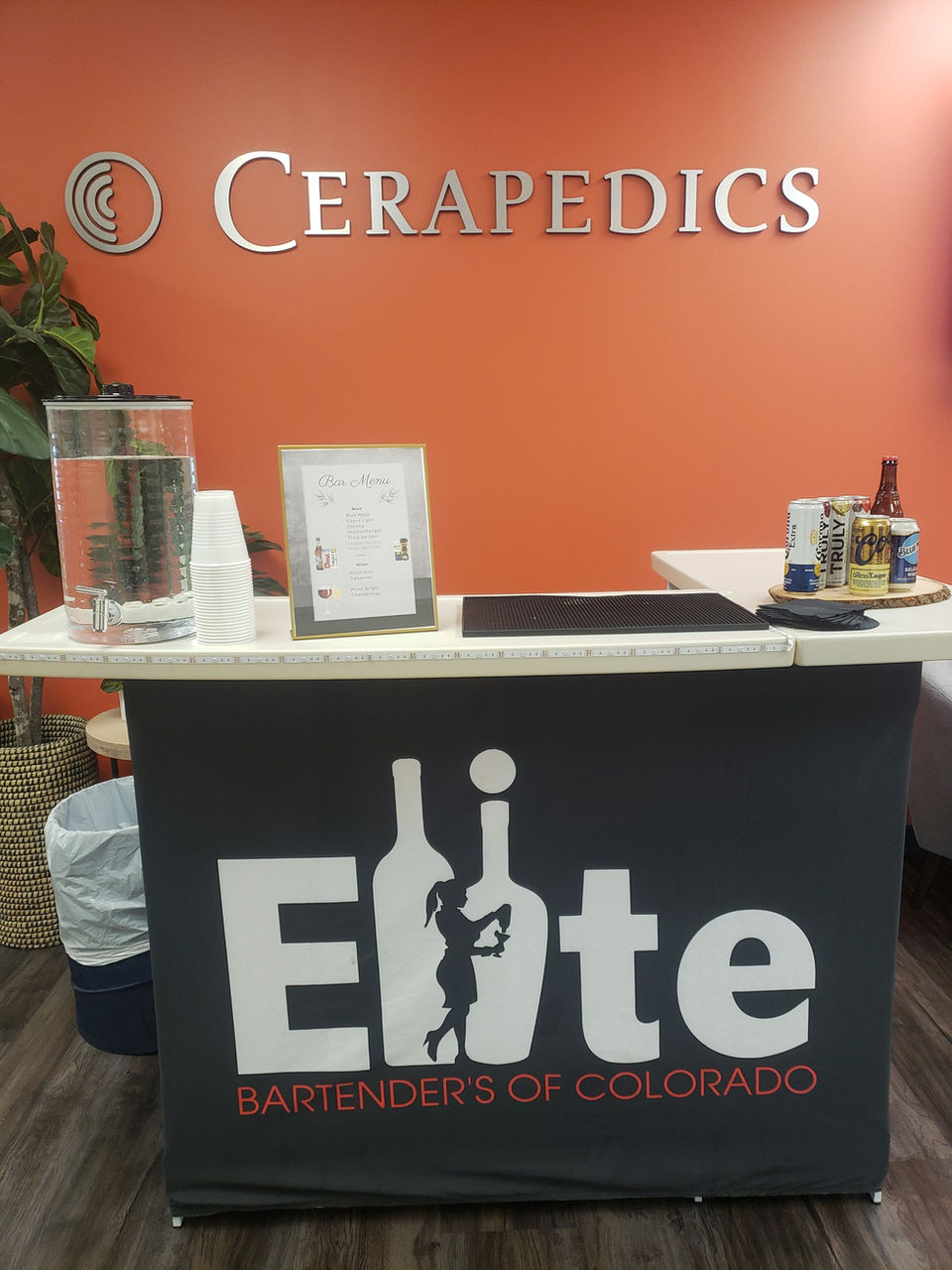 Small black bar with white top that says Elite Bartenders of Colorado on the front with business wall in the backgrounds