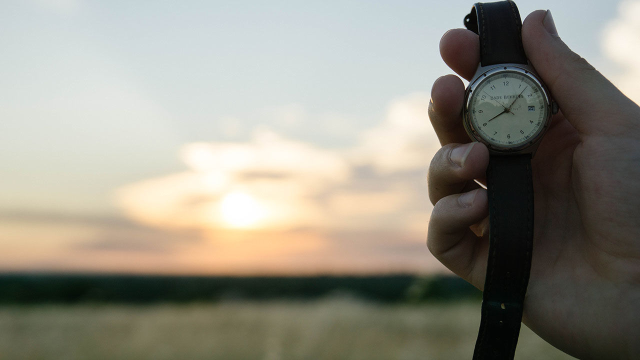 Person holding a watch in front of a sunset.