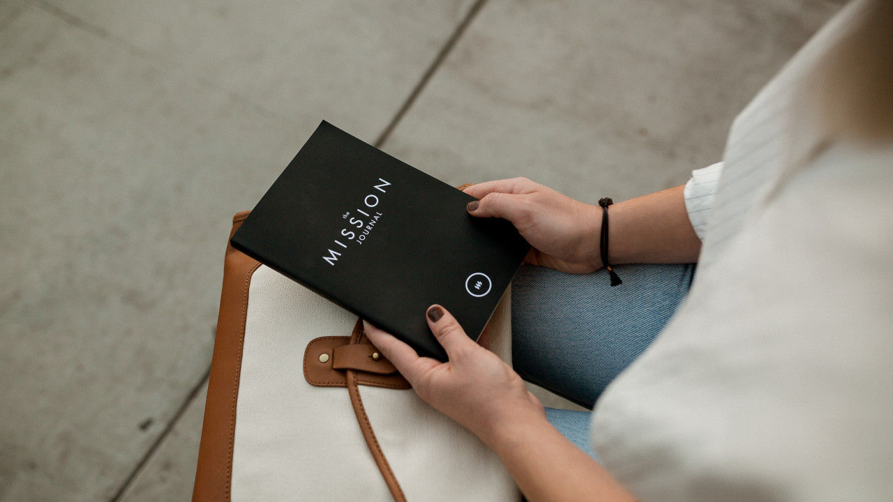 woman holding a notebook in her hands with the word "mission journal" written on it