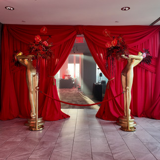 Red fabric-draped entrance flanked by gold statues holding floral arrangements of red roses and anthuriums, leading into the Vue on 50 birthday celebration.