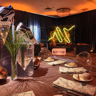 Bar Mitzvah table centerpiece with soccer cleats, grass, and modern lounge area in background.