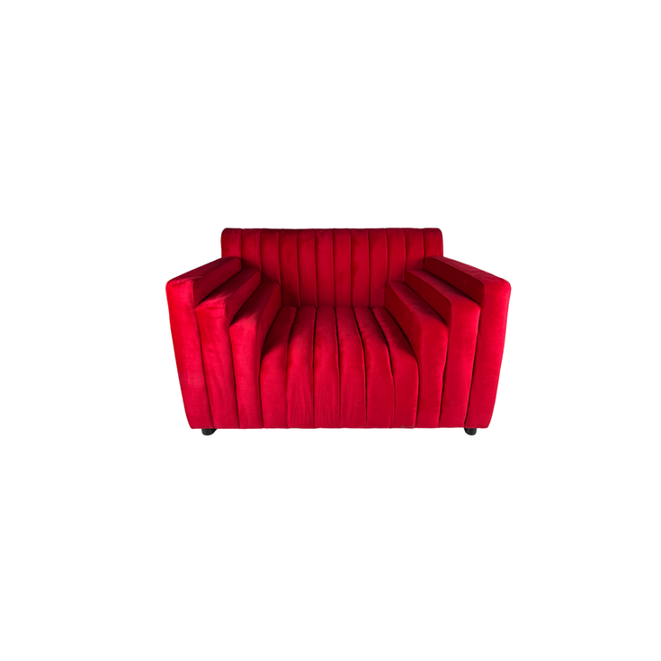 Ruby red velvet lounge chair with vertical channel tufting, wide arms, and a low-profile modern design.