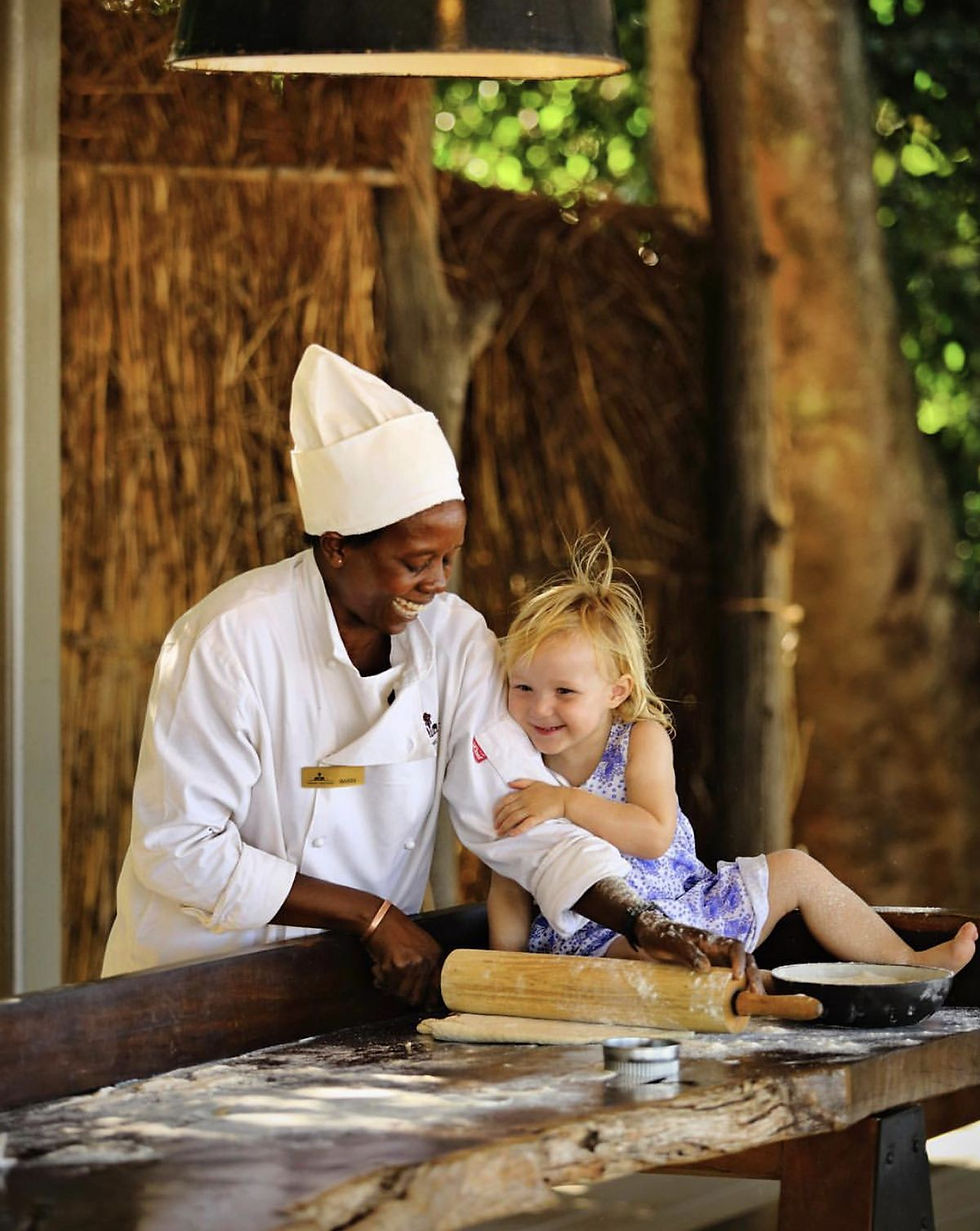 Chef preparing dishes outdoors alongside a young tourist in Rwanda
