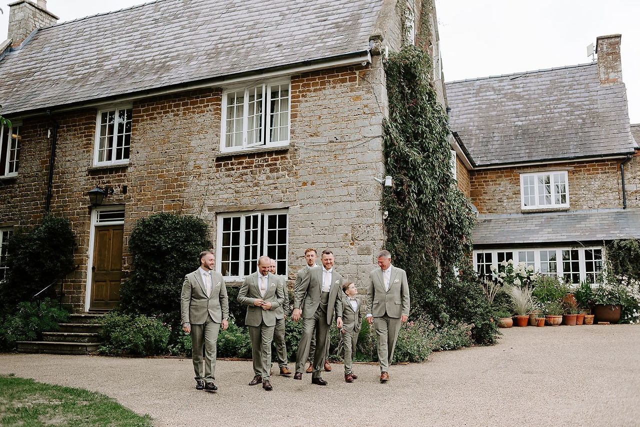 Groom and groomsmen in subtle green suits laughing together before ceremony
