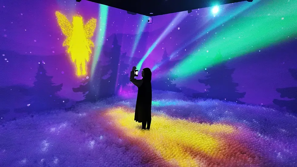 seorang wanita sedang berada di tengah ruang imersif video mapping dengan memegang lentera dan ada gambar peri bercahaya