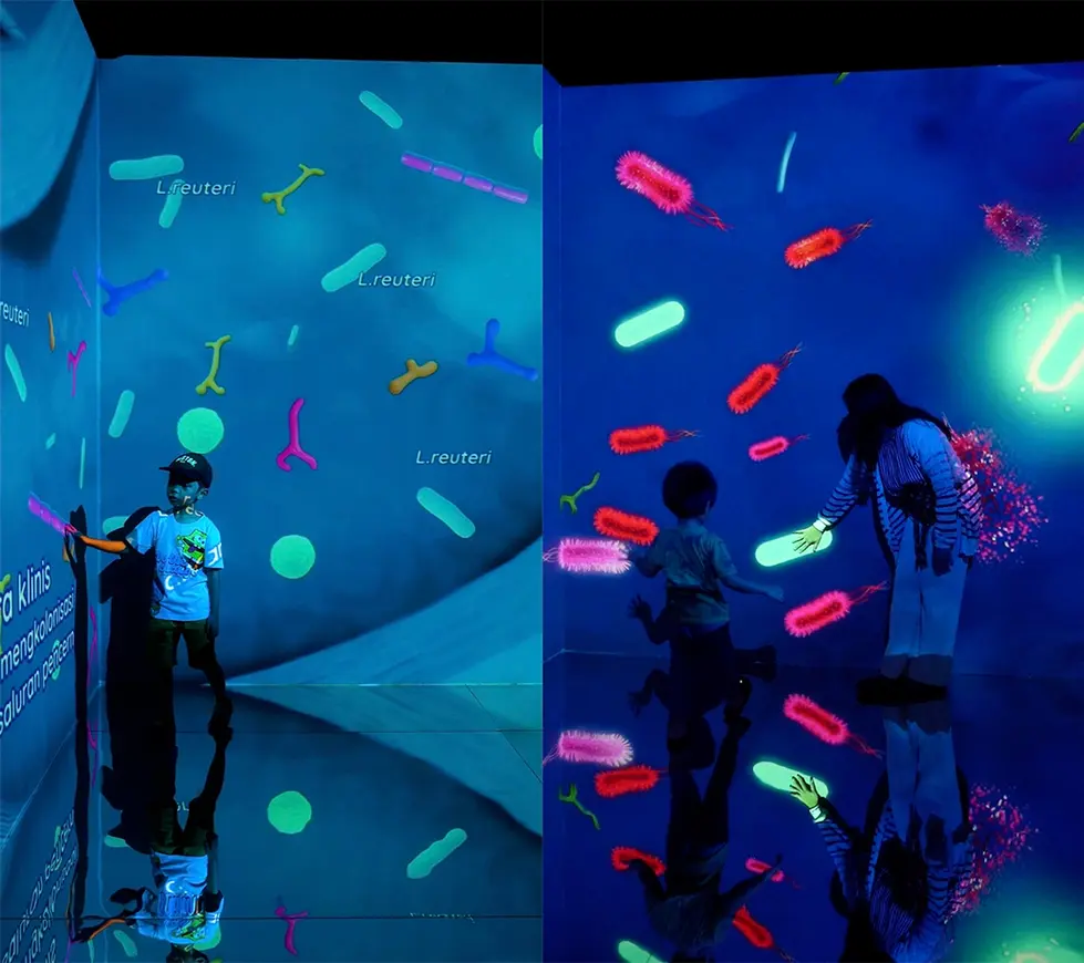 Pengunjung berinteraksi dengan dinding proyeksi menggunakan sensor sentuh di instalasi LZY Visual The Gut Story.