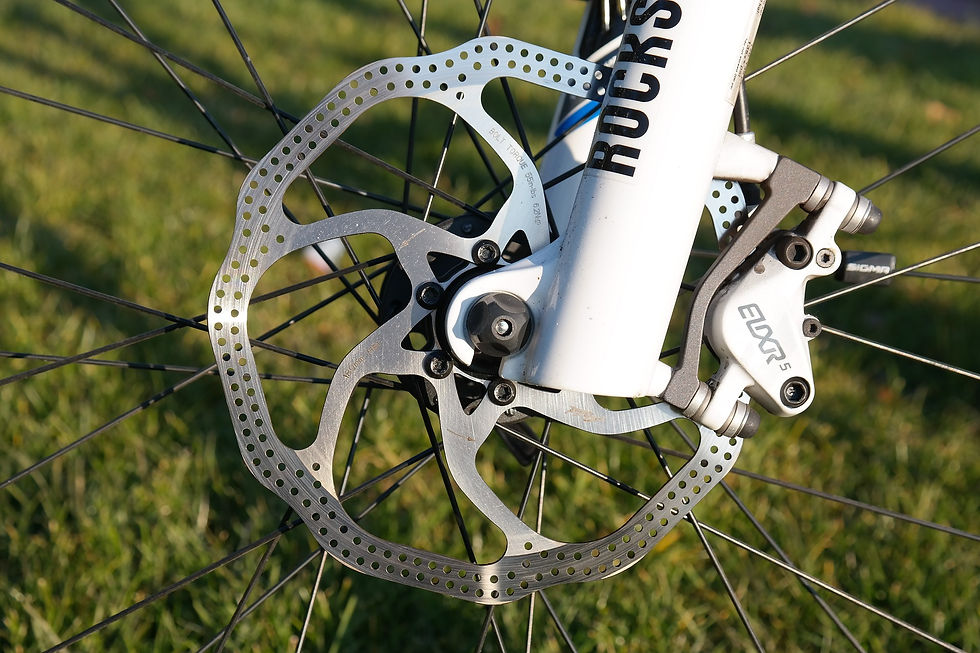 closeup of a disc brake, which is a thin metal disc mounted to the wheel around the hub. The disc runs through a white brake caliper.