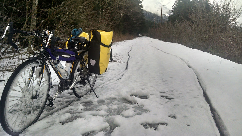 black and green road bike with yellow pannier bags in wet snow that cakes the spokes on the wheel