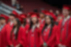 A group of five students dressed in graduation gowns with a young woman in the middle smiling and waving