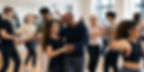 Diverse adults dance in pairs in a bright studio, smiling and turning together in a lively class.
