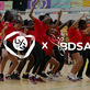 A group of dancers in red shirts perform energetically on a sports court. "LYG x BDSA" logos overlay. Colorful banners adorn the background.