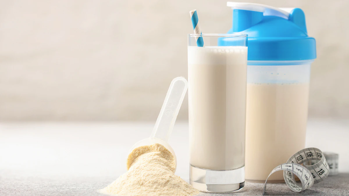 A protein powder scoop next to a protein shake in a cup and bottle shaker.
