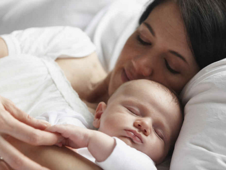Madre dando confort al bebé abrazándolo en tanto ambos descansan plácidamente.