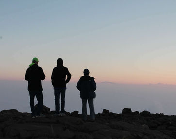 Three people standing on the edge of a mountain watching the sunrise