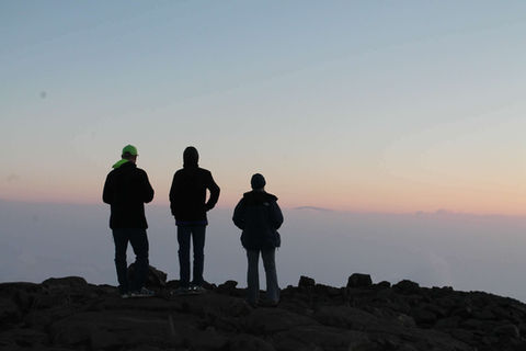 Three people standing on the edge of a mountain watching the sunrise