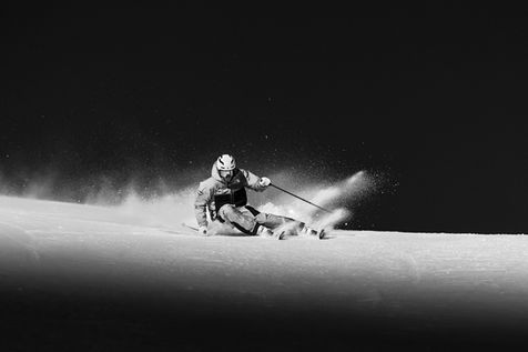 Professionelt sort-hvidt billede af en skiløber i fuld carving på en sneklædt piste, med sne, der flyver op i dynamisk bevægelse. Perfekt til action- og sportsfotografi