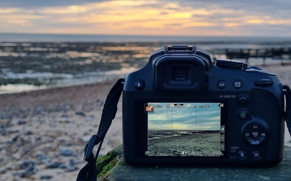 A camera with a sunset in front, on a beach.