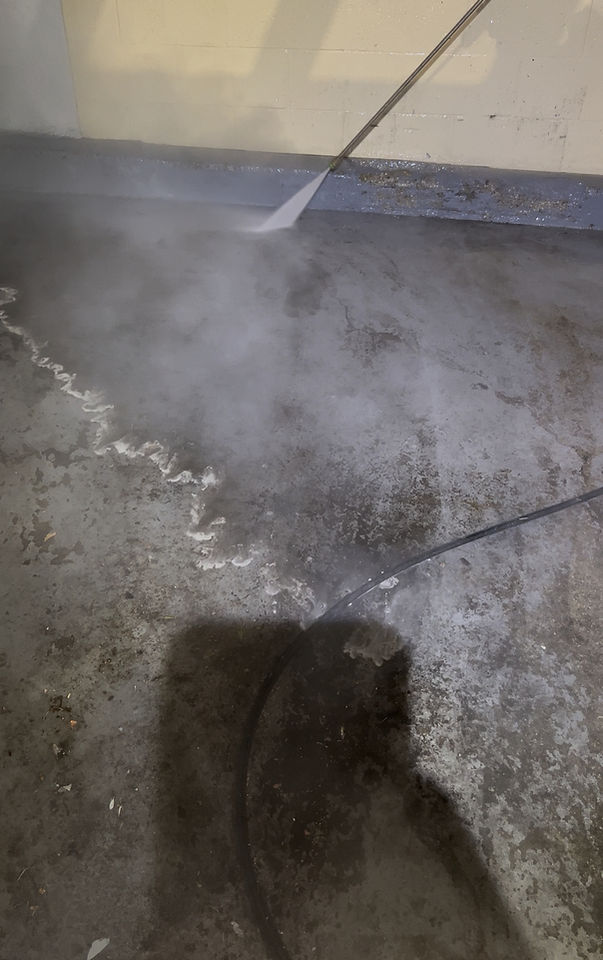 Industrial hot water pressure washing removing heavy grease from a commercial dumpster pad in Inglewood, CA.