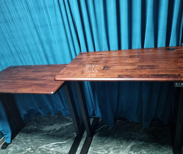 Two wooden desks with black legs are set against blue curtains. The surface is polished brown. Text reads "my-desk.co" on the right desk.