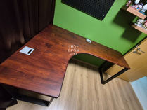 Custom L-shaped corner desk in solid walnut wood. Features an ergonomic curved inner corner for wraparound workspace and a sit-stand adjustable frame.