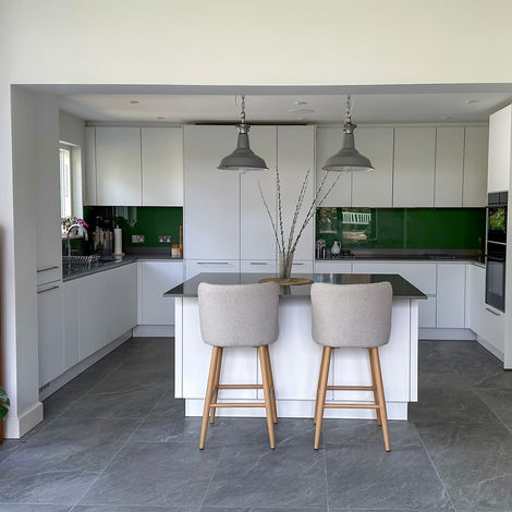 Modern white kitchen with a sleek island, green glass splashback and upholstered bar stools
