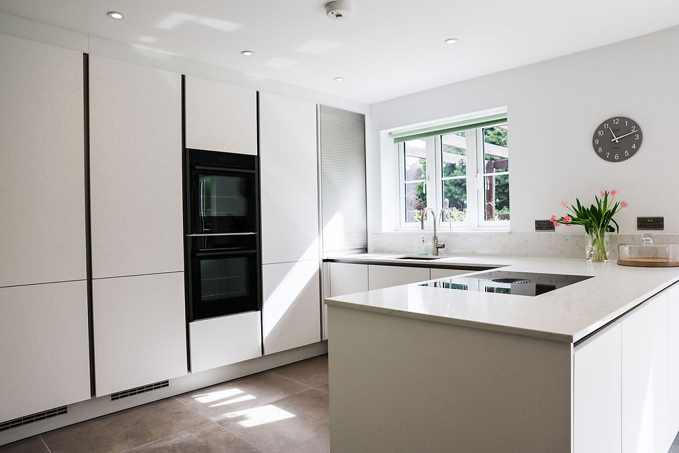 White handleless kitchen with island-style worktop, integrated hob and built-in ovens