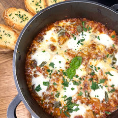 Cheese topped pan of lentil lasagne with garlic bread slices