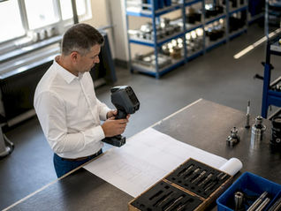 En ingenjör granskar en 3D-skanner vid en arbetsbänk i industrimiljö.