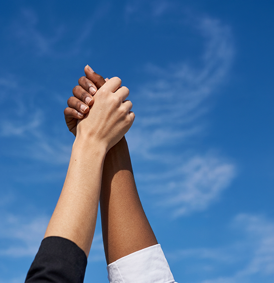 Deux mains de femmes (une caucasienne et une afro-américaine) serrées et levées vers un ci