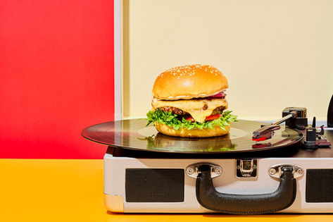 conceptual cheeseburger food photography, set on a split red and yellow backdrop, cheeseburger set on a vinyl player , food photography , North Yorkshire