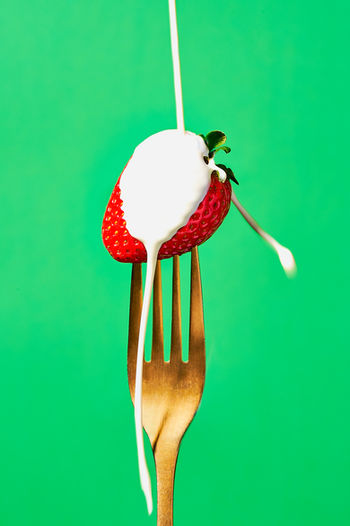 strawberry on a golden fork food photography set on a green backdrop with a splash of cream hitting the strawberry, food photography, North Yorkshire 