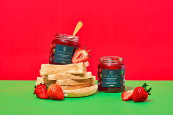 Exceptional by Asda Strawberry Conserve jars styled on a stacked bread tower with fresh strawberries against a bold red and green colour-on-colour backdrop, food and drink photography by Florian Frickel