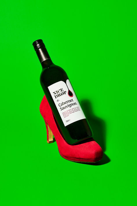 Bottle of Nice Drop Cabernet Sauvignon resting in a red suede heel, shot against a bold green backdrop. Food and drink photography by Florian Frickel