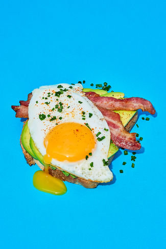 creative avocado on toast with bacon and fried egg set on a bold blue background, commercial food photography, North Yorkshire 