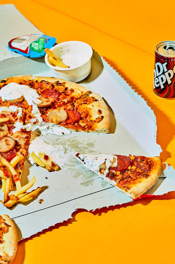 creative commercial photography of ripped pizza box with pizza, fries and a can of Dr Pepper set on orange background, North Yorkshire