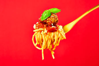Fork twirled with spaghetti bolognese and fresh basil on a vivid red background — bold editorial food photography Yorkshire